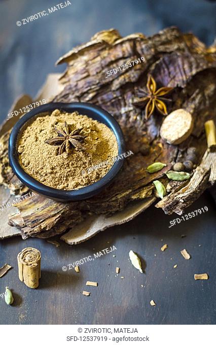 Homemade pumpkin pie spice mix in small bowl on a tree bark