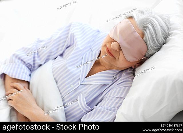 senior woman with eye mask sleeping in bed at home