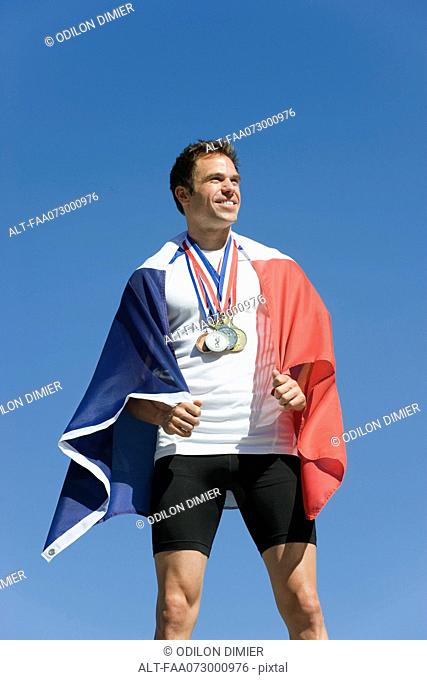 Male athlete being honored on podium, wrapped in French flag