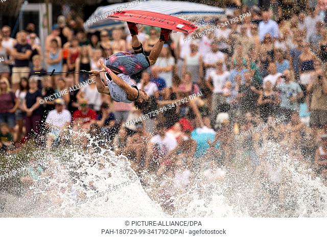 29 July 2018, Germany, Cologne: A wakeboarder jumping over a wave and showing a trick while being pulled by a boat at the wakeboard festival ""Eat Play Love""