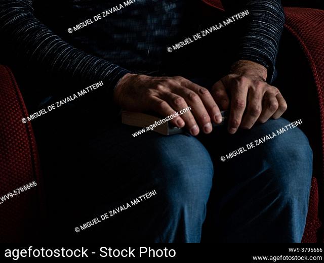 A pair of man's hands hold a book sitting in his favorite couch