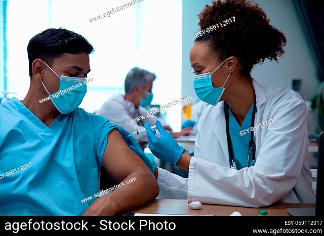 Mixed race couple of doctors wearing face masks making injection
