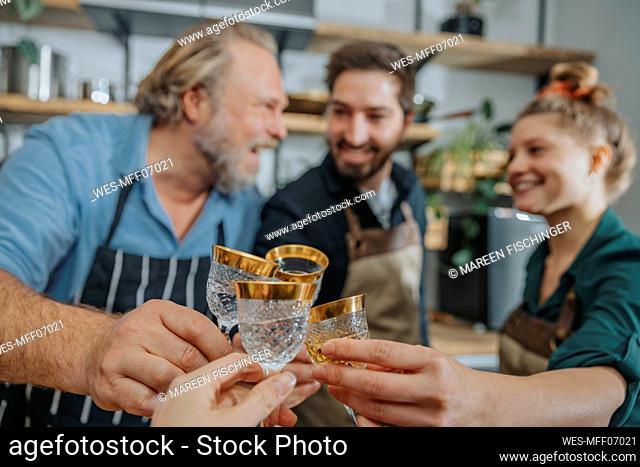 Chefs toasting drinks with woman while standing in kitchen