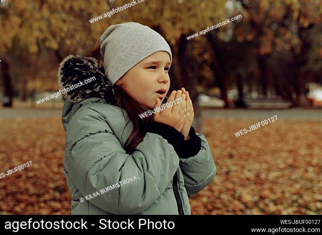 Girl wearing knit hat warming hands at autumn park