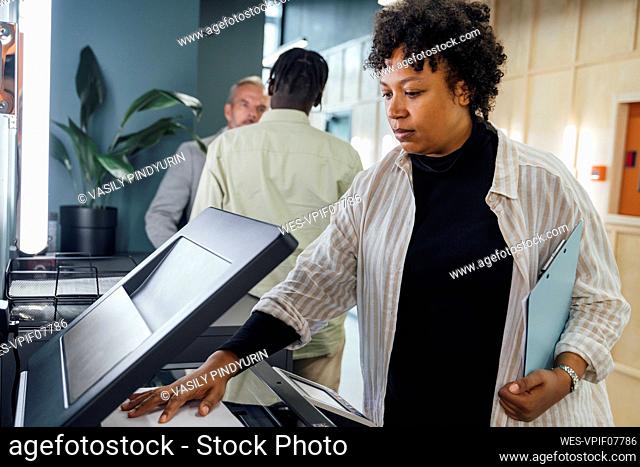 Young businesswoman using photocopier machine with colleagues standing in background