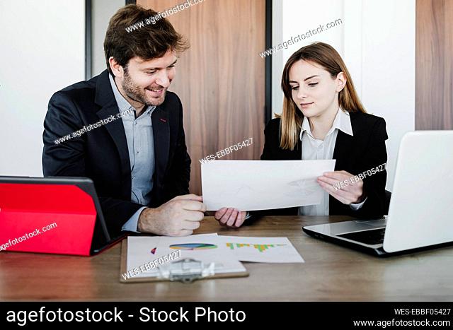 Businesswoman discussing report with colleague sitting at desk in office