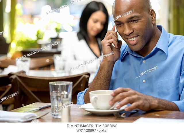 Business people outdoors, keeping in touch while on the go. Two people sitting at coffee shop tables, checking their messages