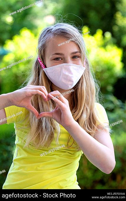 Girl wearing protective mask and forming a heart with her hands outdoors
