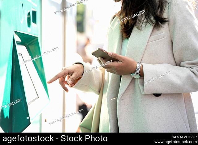 Close-up of woman using ticket machine at tram stop