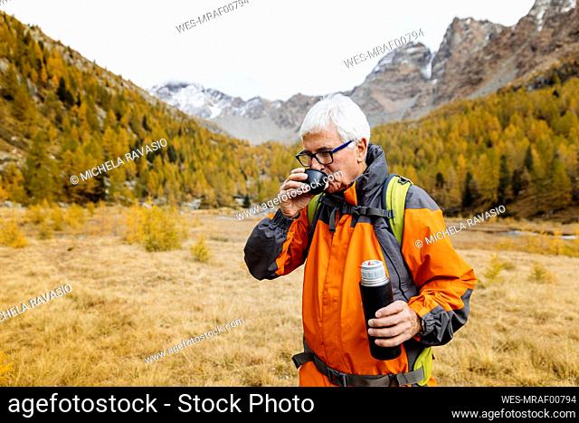 Senior hiker drinking coffee on grass at Rhaetian Alps, Italy