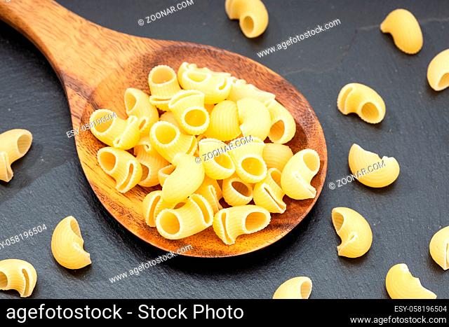 Uncooked elbows macaroni pasta in wooden spoon on dark table