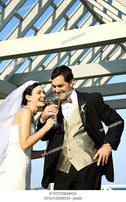 Caucasian mid-adult bride and groom drinking champagne