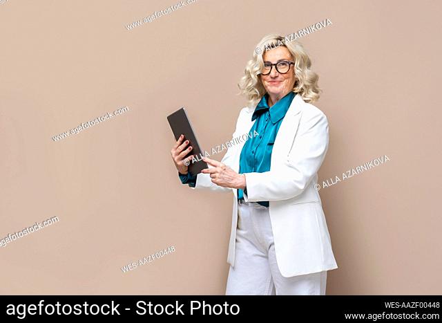 Senior businesswoman holding tablet PC against colored background