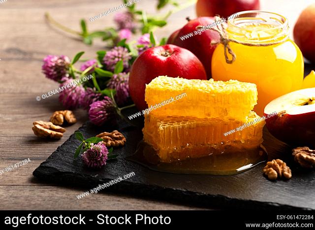 Mason jar with honey, honeycomb, red apples and walnuts on kitchen table