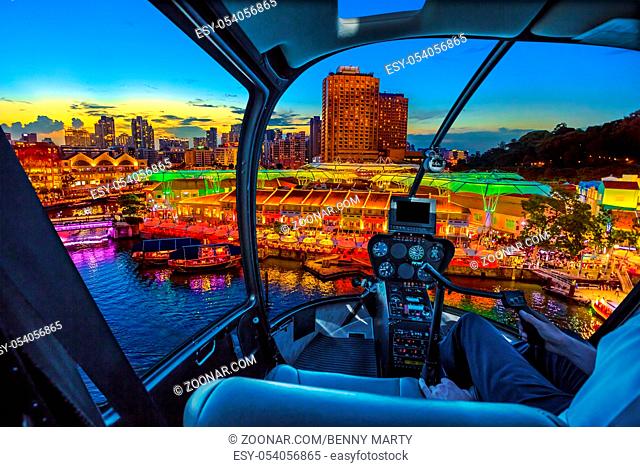 Helicopter cockpit interior flying on aerial skyline of Clarke Quay and riverside area at sunset in Singapore, Southeast Asia
