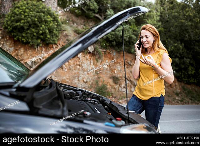 Woman talking on mobile phone for roadside assistance while standing by car