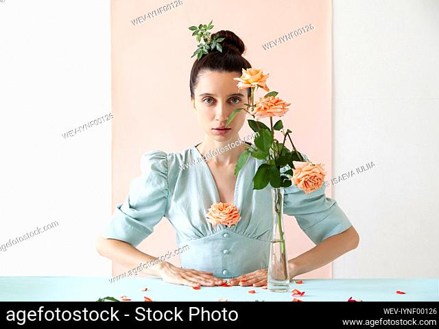 Beautiful young woman with rose in vase against pink backdrop