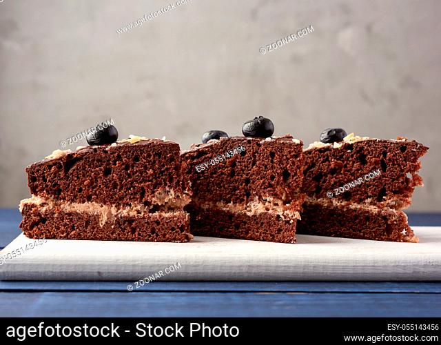 three triangular pieces of chocolate biscuit cake with butter cream on a white wooden board, gray background