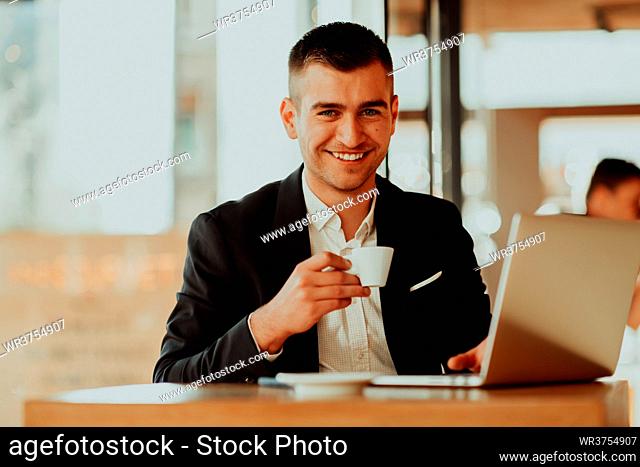 businessman sitting at the cafeteria with a laptop and smartphone. Businessman texting on smartphone while sitting in a pub restaurant