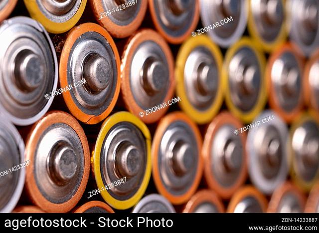 Multiple used AA alkaline batteries are seen arranged in a pile. Closeup side view from the plus side of the battery