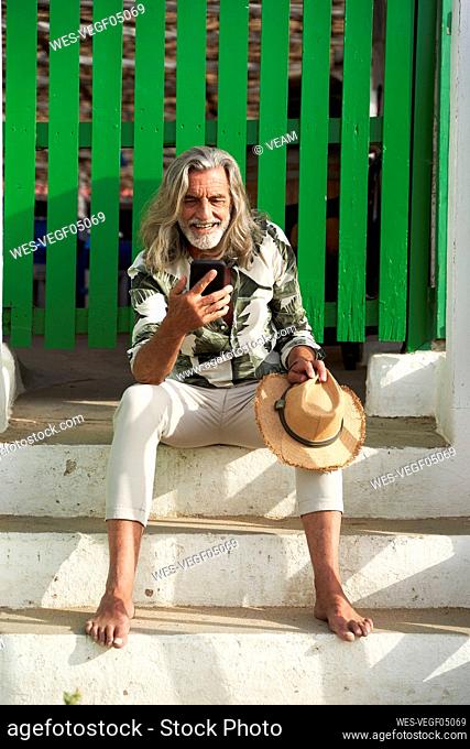 Smiling mature man doing video call through mobile phone on steps