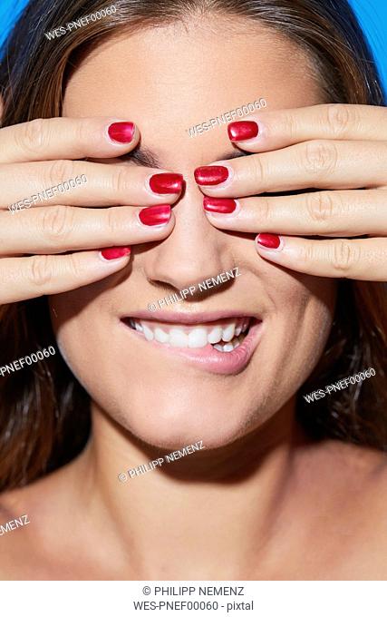 Beautiful young woman with red fingernails covering her eyes