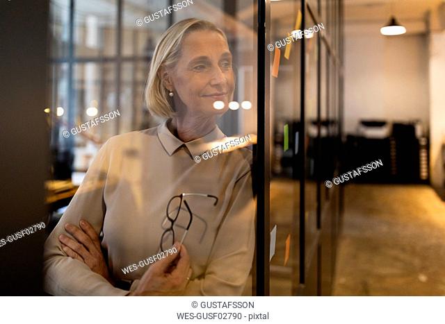 Mature businesswoman looking at adhesive notes on glass pane in office