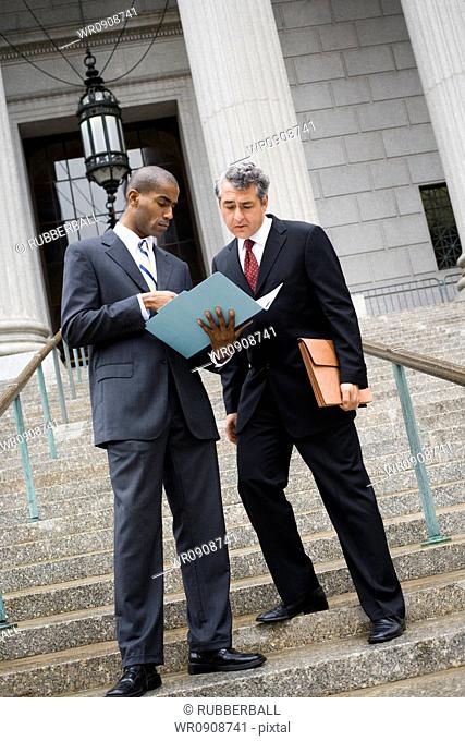 Low angle view of two men looking at documents on the steps of a courthouse