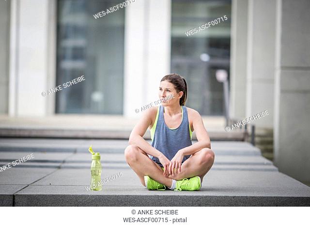 Sportive woman sitting on ground with drinking bottle