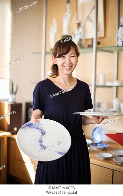 Smiling woman standing in a Japanese porcelain shop, holding two white plates with blue decoration