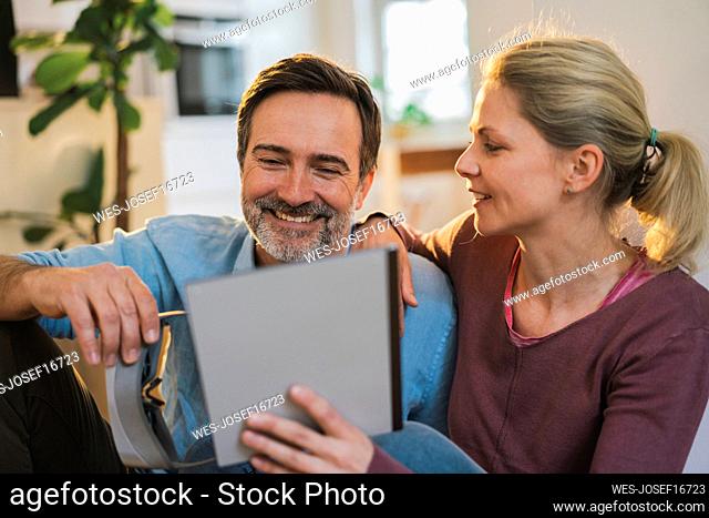Smiling man looking at tablet PC held by woman at home