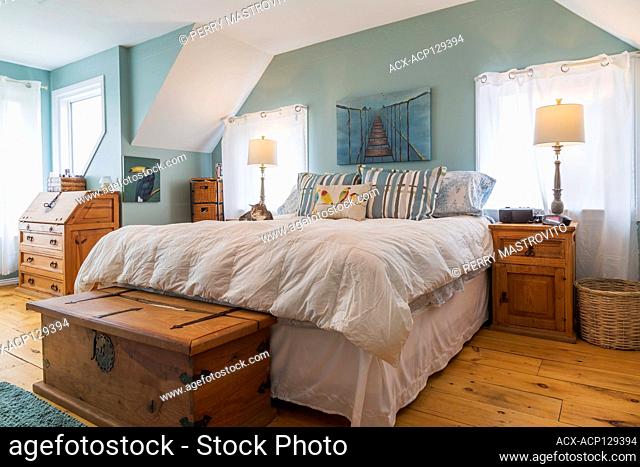 Queen size bed with pinewood nightstands, chest, secretary desk in upstairs master bedroom with wide pinewood plank floorboards inside an old circa 1830...