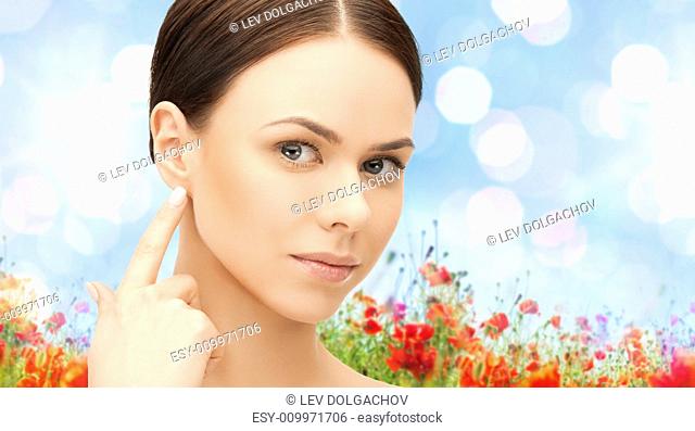people, beauty, hearing and healthcare concept - face of beautiful woman touching her ear over poppy field background
