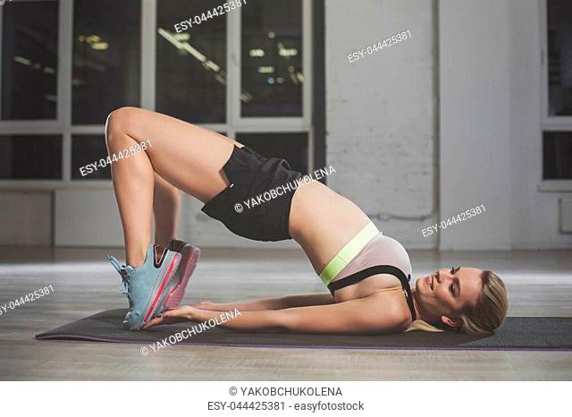 Full length of girl working out on her own. She is lying on back while pushing body up with concentration and smile