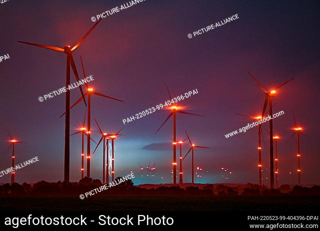 20 May 2022, Brandenburg, Jacobsdorf: The red position lights on wind turbines illuminate the night sky, while lightning from a thunderstorm can be seen behind...