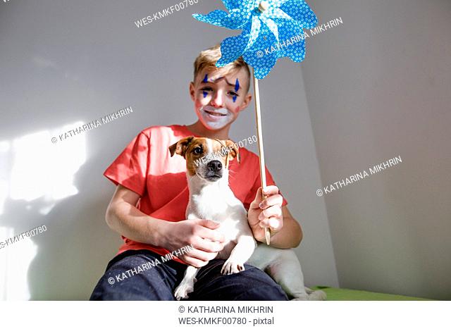 Portrait of Jack Russel Terrier with boy made up as a clown holding pin wheel