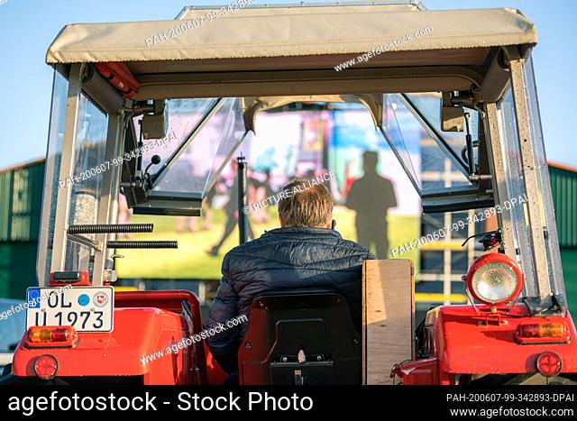 07 June 2020, Lower Saxony, Hude: In the evening, a farmer sits in his tractor on a large meadow and watches the documentary ""The Beautiful Krista"" about a...