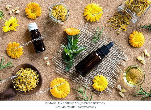 Two bottles of essential oil, calendula (marigold), thyme, rosemary and frankincense on a brown background, top view
