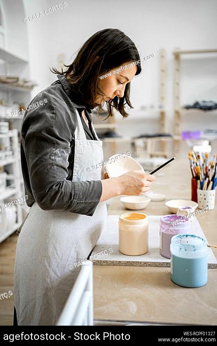 Young craftswoman painting on bowl in workshop