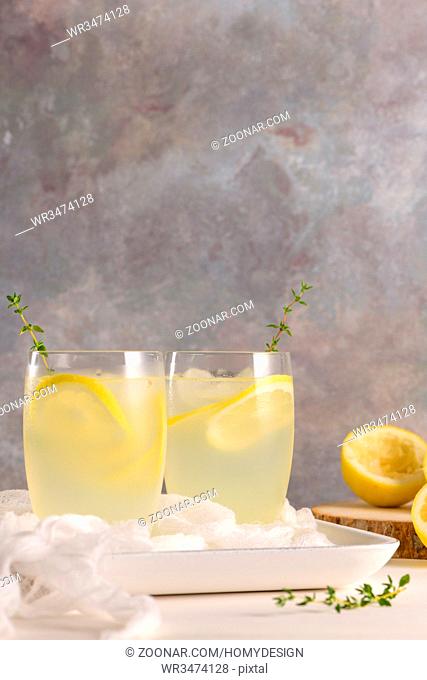 Cold lemonade or alcoholic cocktail with lemon, rosemary and ice in glass glasses on a light background