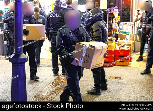 25 November 2023, North Rhine-Westphalia, Wuppertal: Customs staff carry boxes of possible evidence out of a store. Heavily armed police officers searched eight...