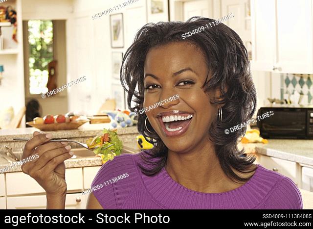 Smiling Black woman eating salad in kitchen
