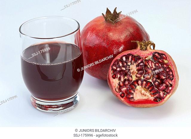 Pomegranate (Punica granatum), whole and halved fruit with a glass of juice. Studio picture against a white background