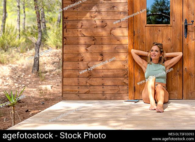 Smiling woman with hands behind head leaning on door at porch