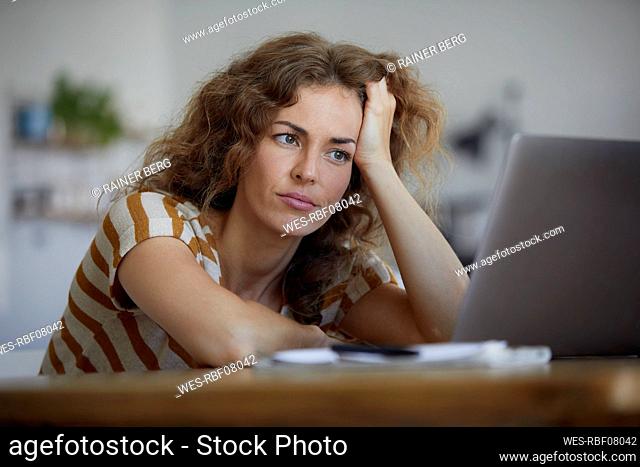 Tired woman with head in hand sitting by table at home