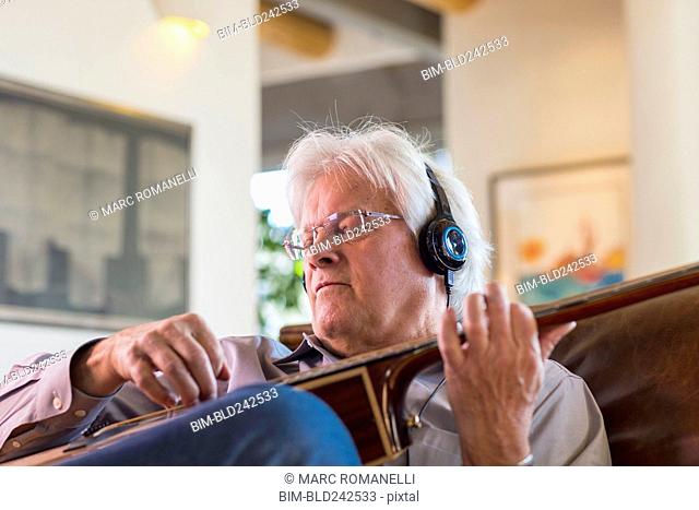 Caucasian man listening to headphones and playing guitar