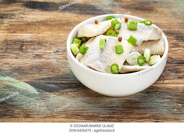 herring in wine with green onion and spices - white sauce dish on a grunge wood
