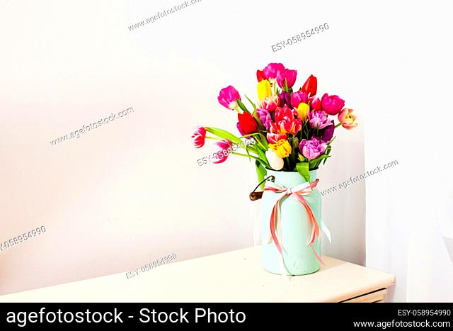 Large fine bouquet of colorful tulips in white can with wooden handle and pink band on neck, isolated on white background