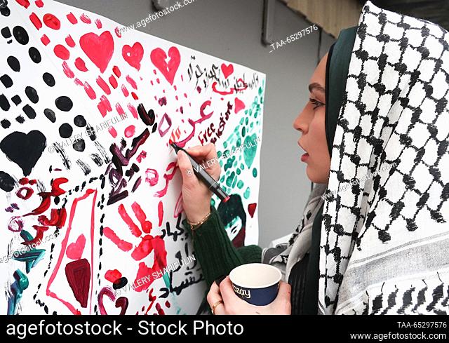 RUSSIA, MOSCOW - NOVEMBER 28, 2023: A woman wearing a Palestinian keffiyeh writes a message outside the Palestinian Embassy on the International Day of...