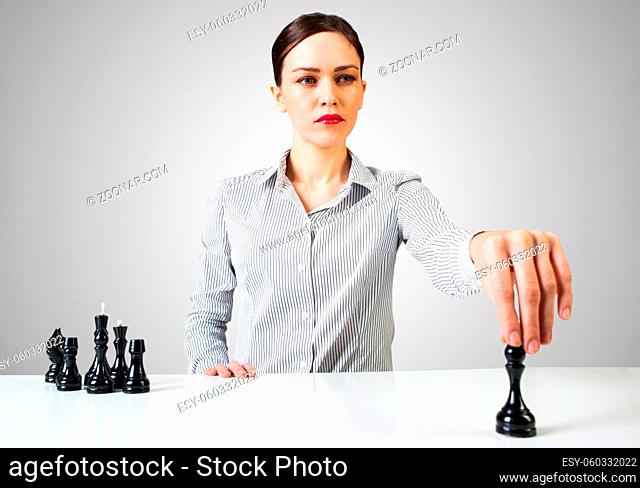 Confident businesswoman playing chess at desk. Portrait of girl with bright red lips on white wall background. Intellectual duel and tactical battle in business